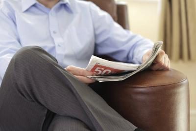 Un homme lit le journal dans un fauteuil en cuir.