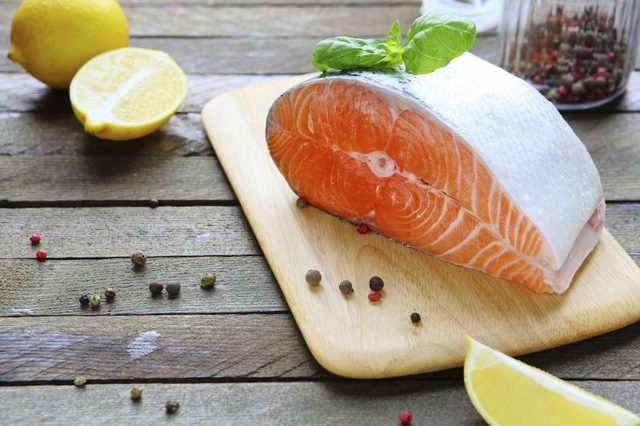 Une tranche de saumon sur une planche à découper avec du poivre et citron.