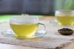 Deux tasses en verre de thé vert chaud plaine avec un petit bol de feuilles de thé séchées.