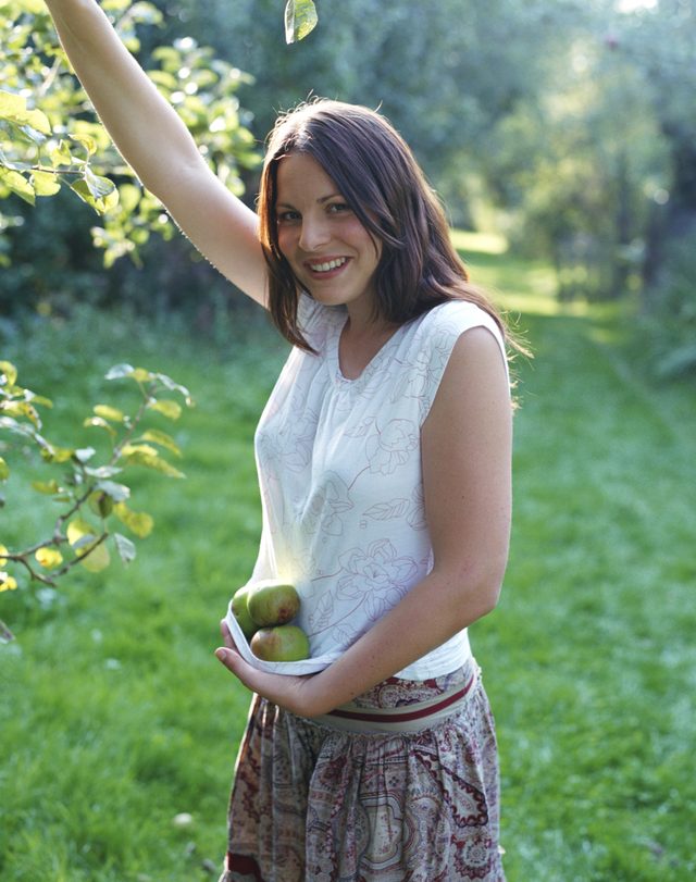 Une femme atteint jusqu'à ramasser une pomme d'un arbre.