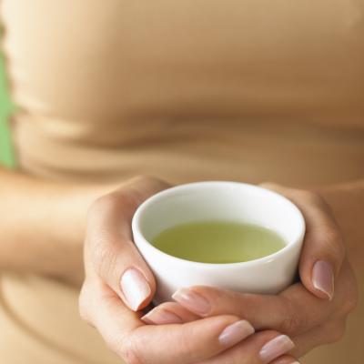 Une femme tient une tasse de thé vert chaud.
