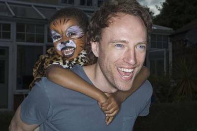 Un homme joue avec une peinture de visage de l'enfant portant.